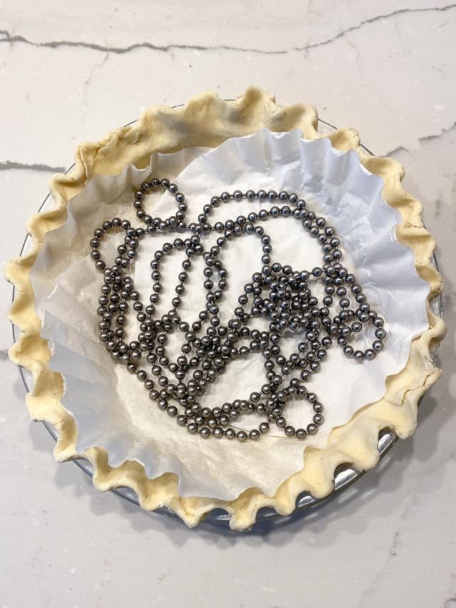 lining unbaked pie crust with coffee filters and pie weights on marble counter