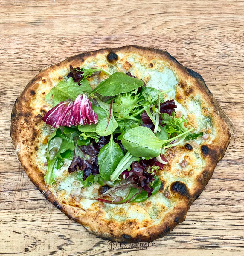 Pesto white pizza topped with salad on wooden board