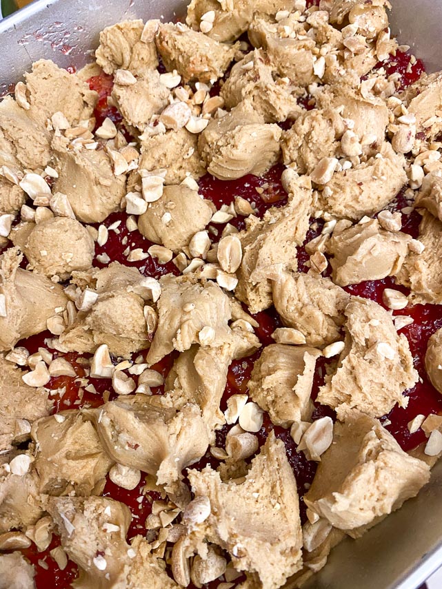 peanuts sprinkled on top of peanut butter and jelly bar batter in pan