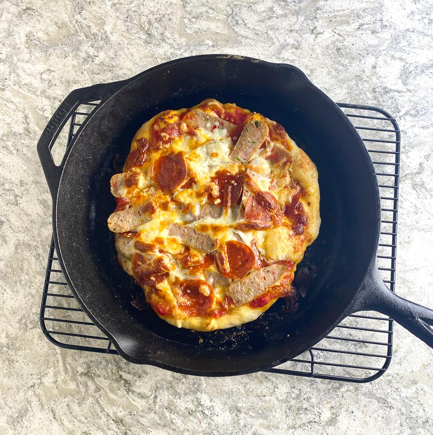 sausage and pepperoni sourdough pizza in cast iron pan on cooling rack