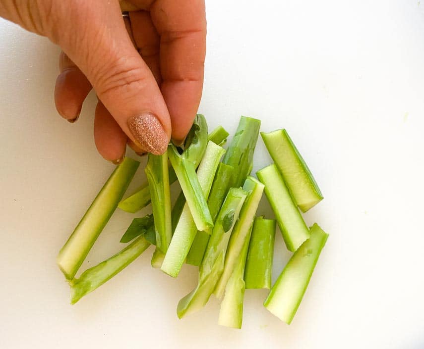 stems from Chinese broccoli cut into smaller pieces on white board with woman's hand