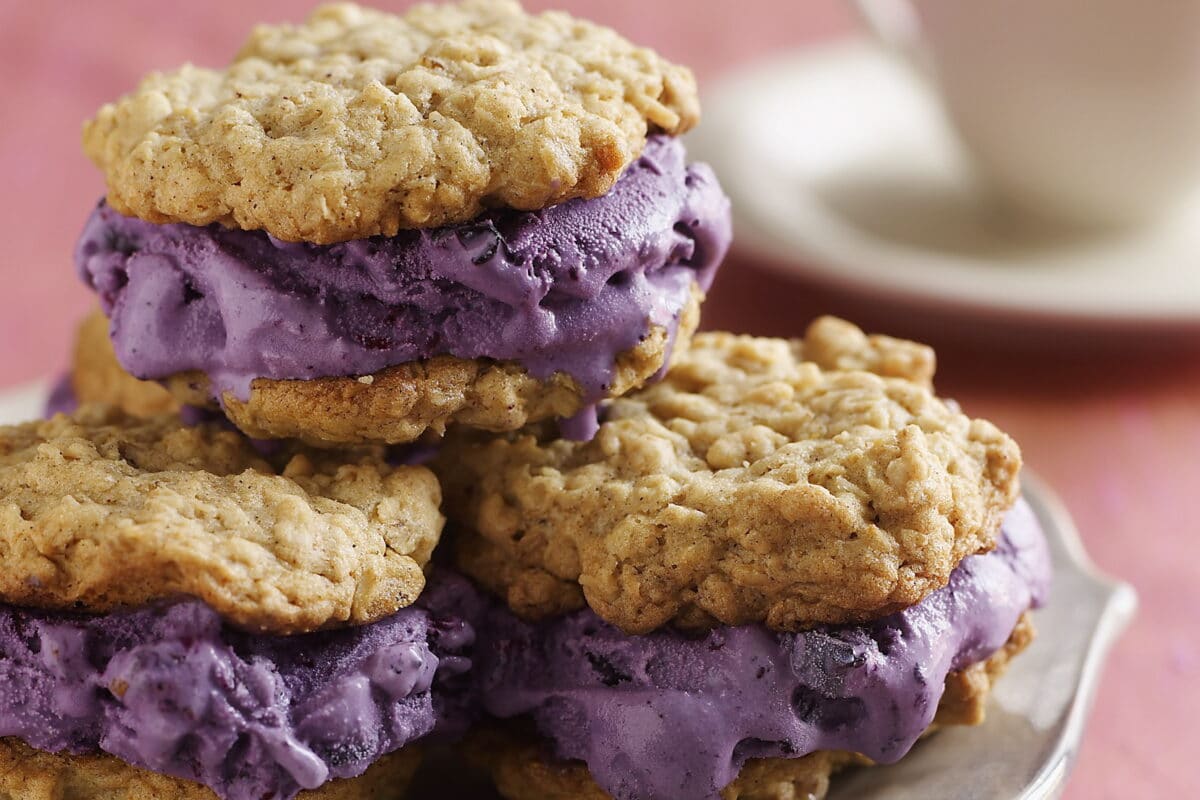 Roasted blueberries folded into lactose-free vanilla ice cream sandwiched between oatmeal cookies stacked on a plate