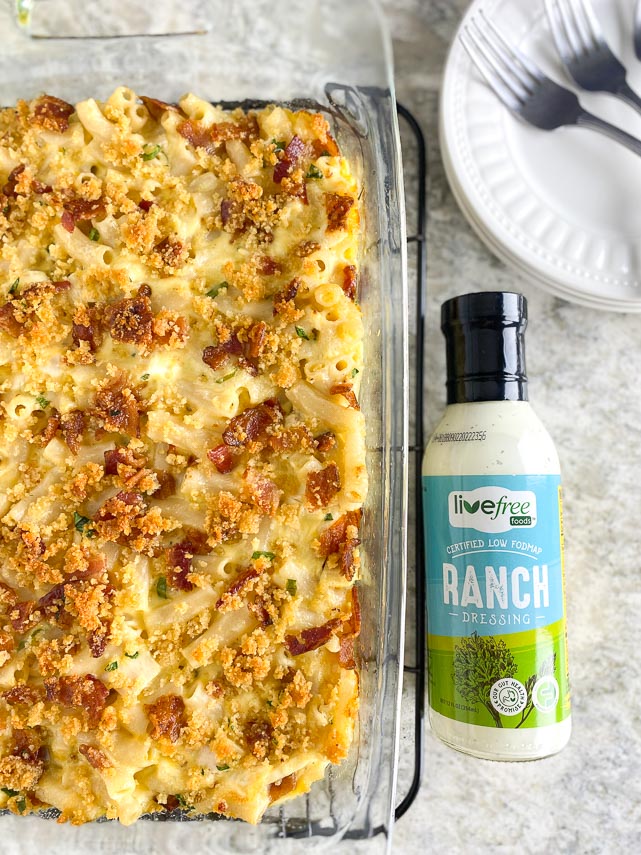 overhead image of Low FODMAP Chicken & Bacon Ranch Mac and Cheese in glass dish, forks alongside with bottle of Dressing