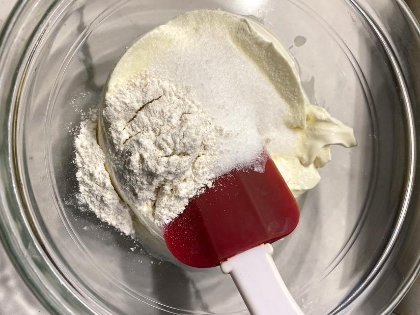 flour, sugar and cream cheese being combined in glass bowl with spatula