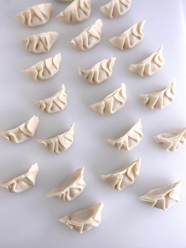 pleated dumplings on white board ready to cook