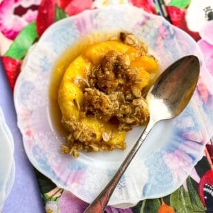 Close Up of Low FODMAP peach crisp on white plate with floral napkins and silver spoons