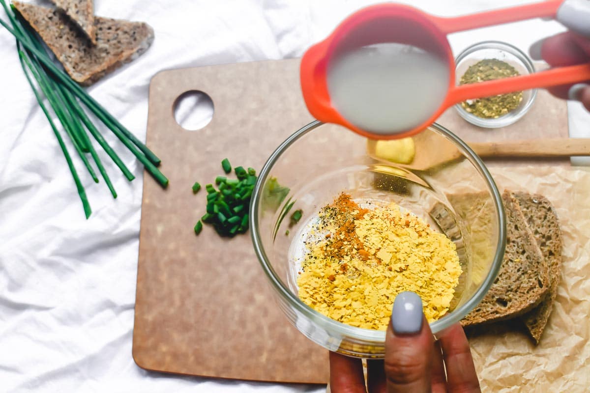 adding rice milk to small bowl of nutritional yeast
