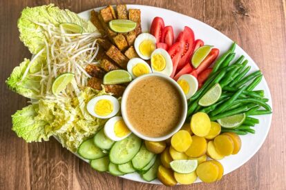 main image of white oval platter holding Low FODMAP Gado-Gado with dishes of shrimp crackers alongside on wooden surface