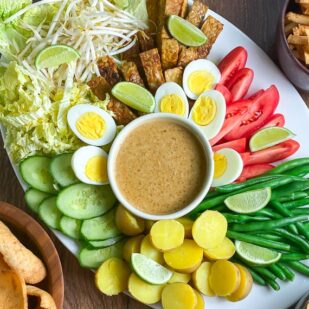 overhead horizontal image of white oval platter holding Low FODMAP Gado-Gado with dishes of shrimp crackers alongside on wooden surface