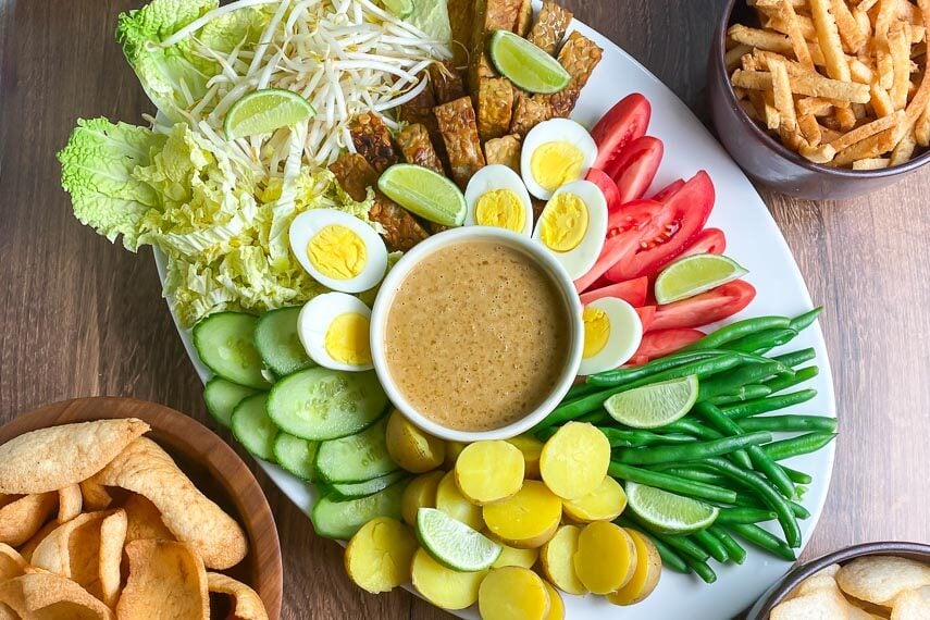 overhead horizontal image of white oval platter holding Low FODMAP Gado-Gado with dishes of shrimp crackers alongside on wooden surface