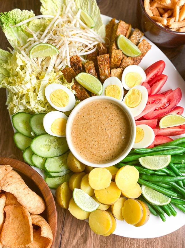 overhead vertical image of white oval platter holding Low FODMAP Gado-Gado with dishes of shrimp crackers alongside on wooden surface