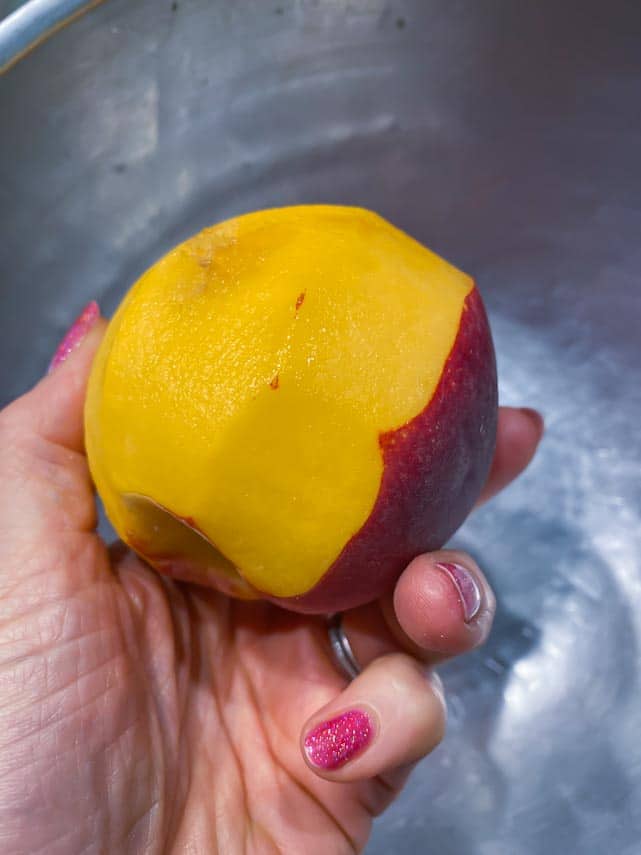 partially peeled peach held in woman's hand over bowl
