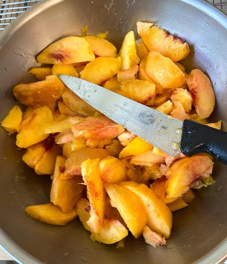 peeled peach wedges cut directly into bowl, shown with knife