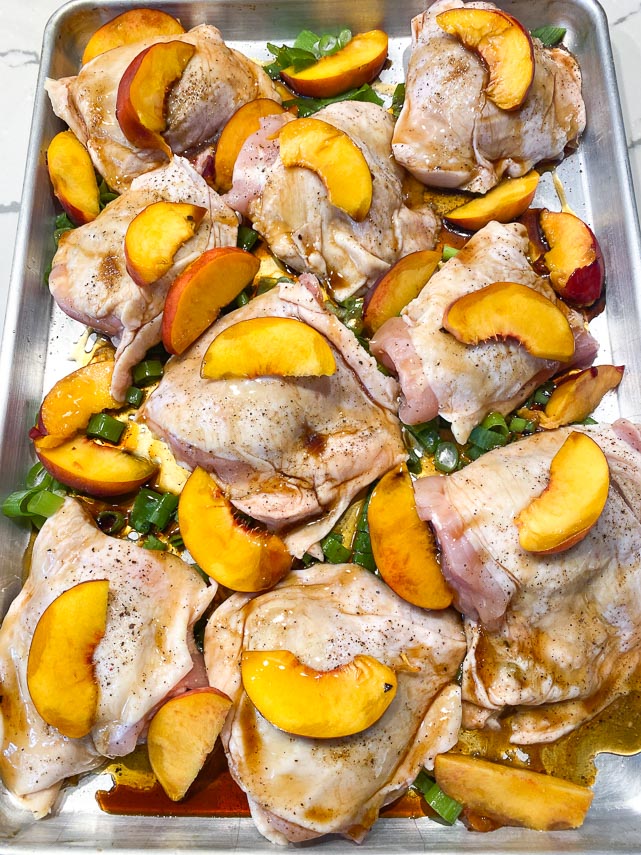 sheet pan holding chicken thighs, peaches and scallions