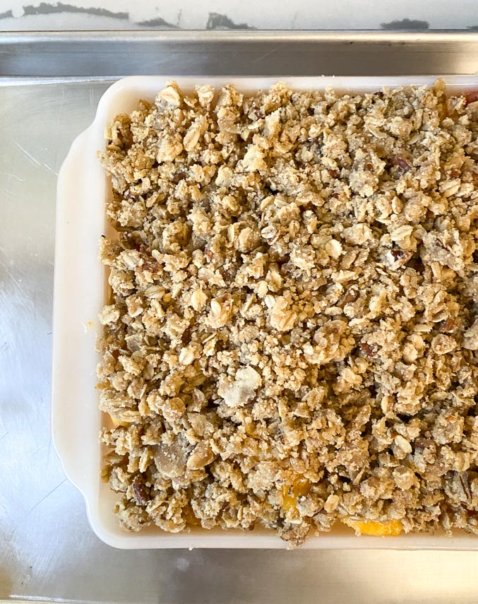 square dish of peach crisp placed on half-sheet pan to catch drips