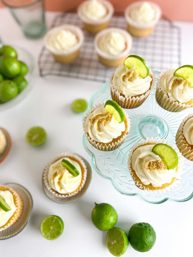 vertical image of Low FODMAP Key Lime Cupcakes on table and aqua cake stand