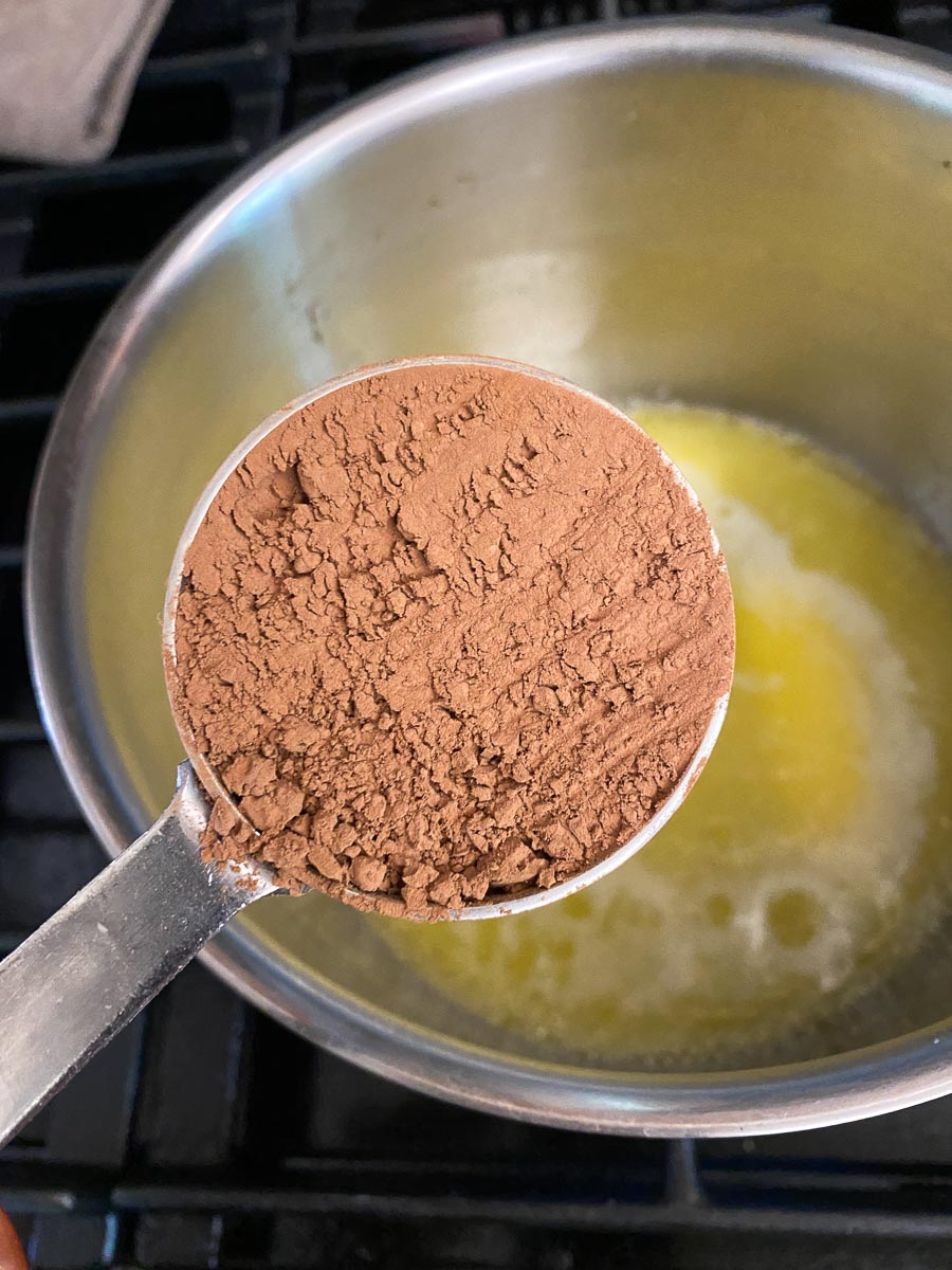 natural cocoa in measuring cup held over pot of melted butter