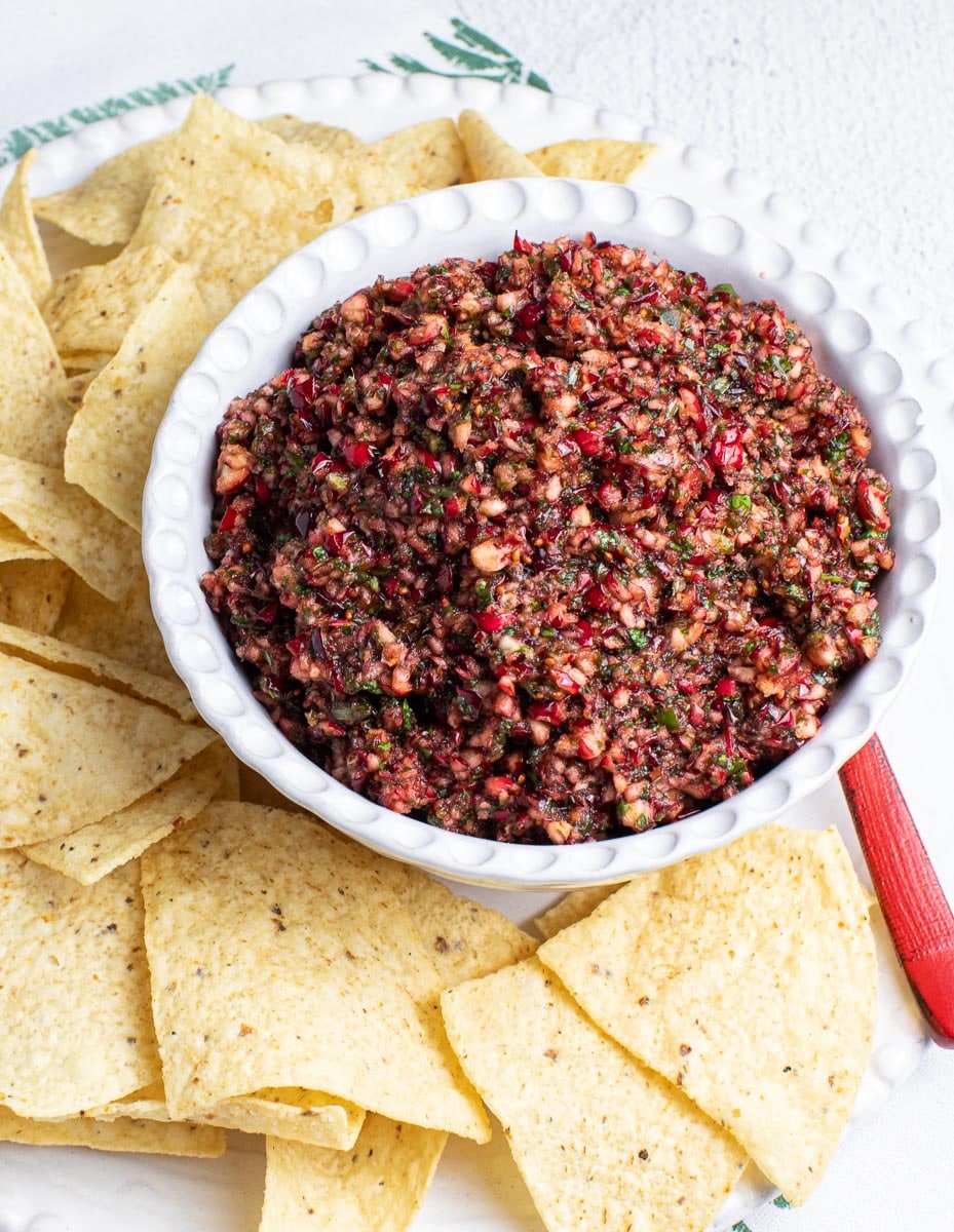vertical low FODMAP Cranberry Salsa in white bowl with chips on placemat