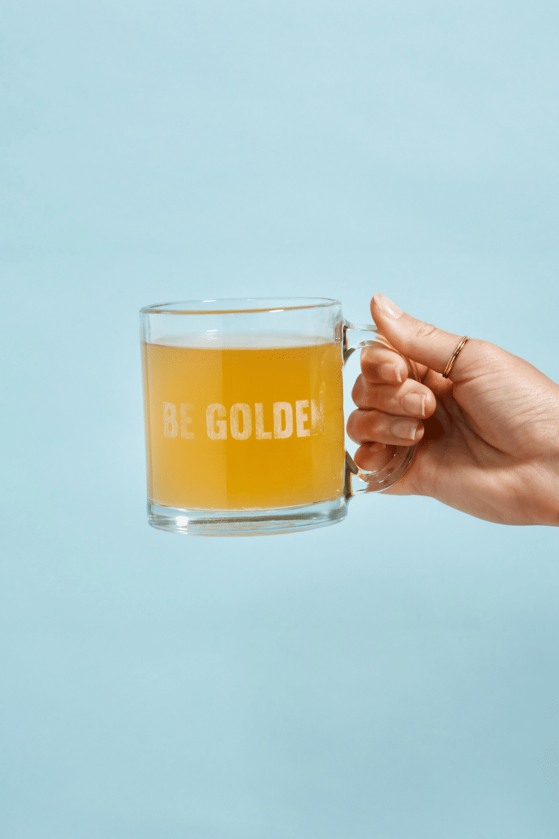 a hand holding a glass cup of golden ratio gold coffee on a blue background