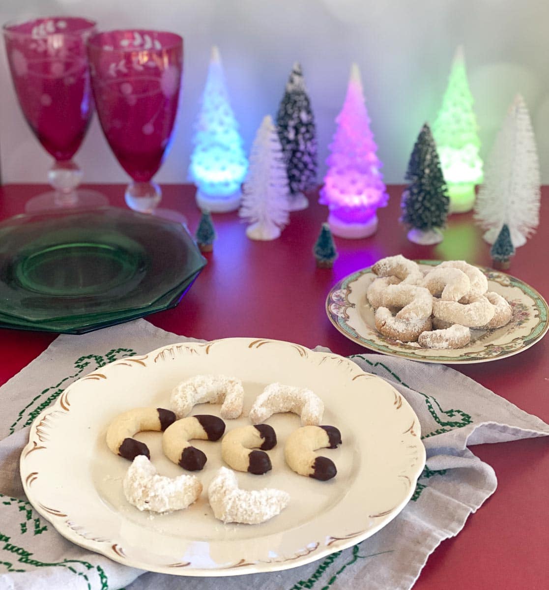 Low FODMAP Vanilla Crescent Cookies on decorative plates; red background and lit Christmas trees