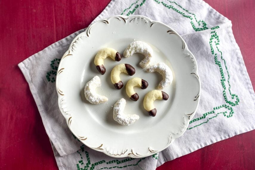 horizontal image of Low FODMAP Vanilla Crescent Cookies on decorative plate; red background. These are hand-shaped gluten-free Christmas cookies.