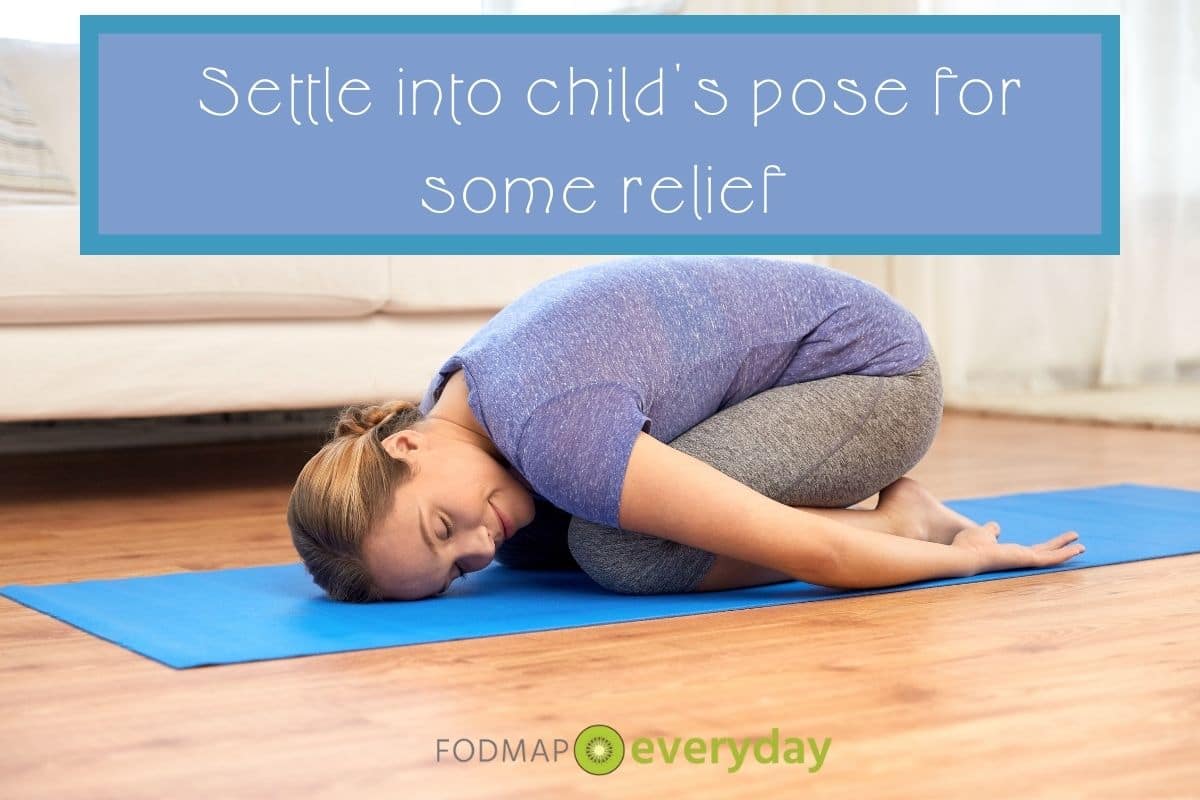 Young woman in yoga gear in 'child's pose" on a blue yoga mat on a wooden floor looking very serene