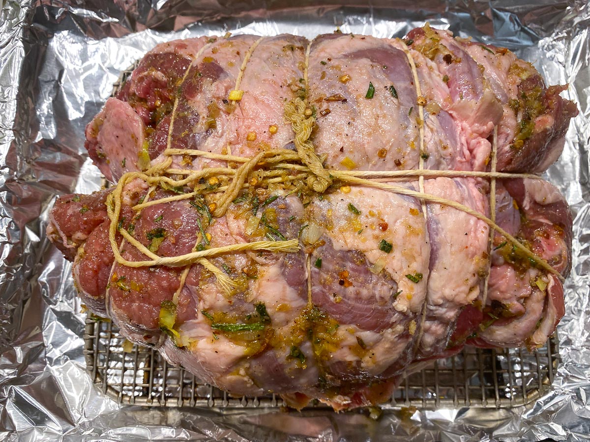 Leg of lamb slathered with lemon and herbs, tied with Butcher twine, on rack in foil lined roasting pan