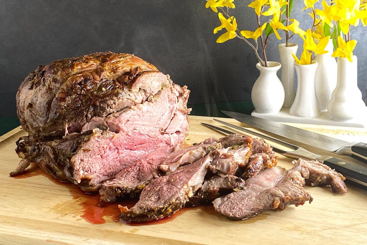 Low FODMAP Boneless Leg of Lamb, carved on wooden board, yellow flowers in background