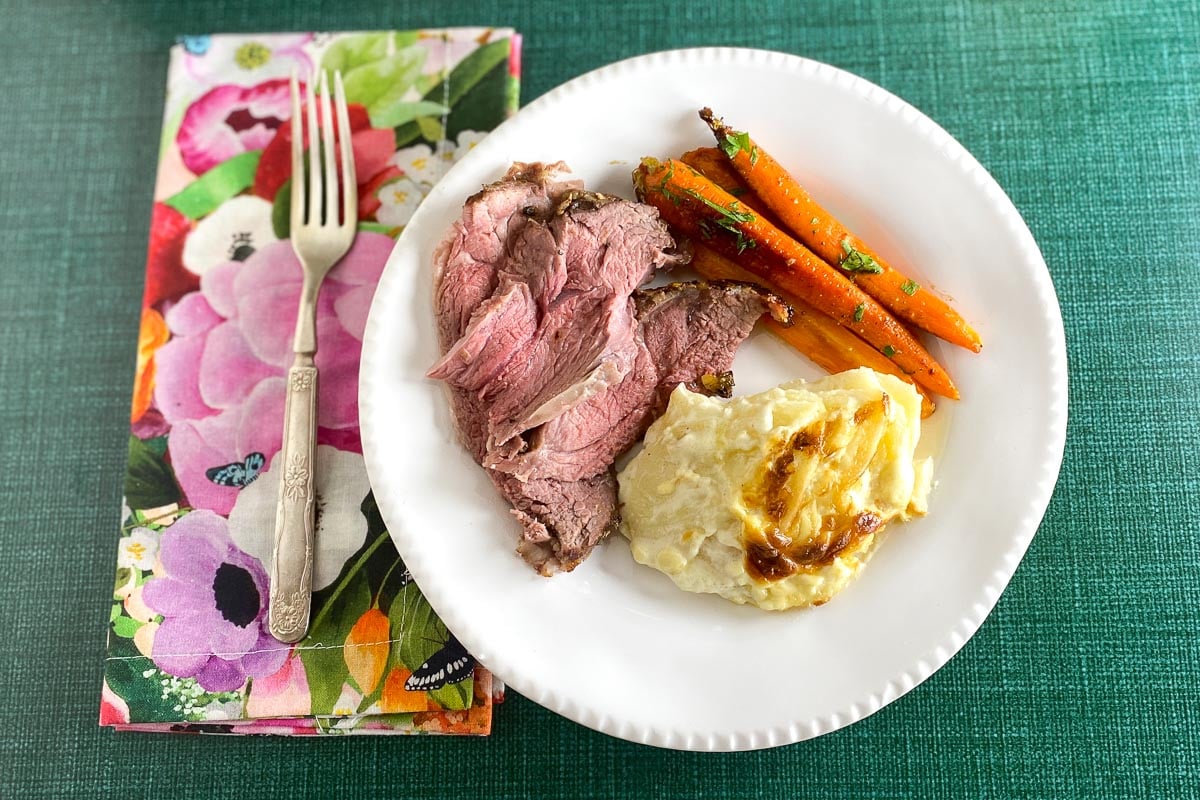 Low FODMAP Boneless Leg of Lamb, plated with scalloped potatoes and carrots on white plate; flowered napkin
