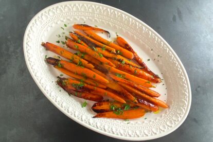 Low FODMAP Honey Lemon Roast Carrots on white oval platter on dark background