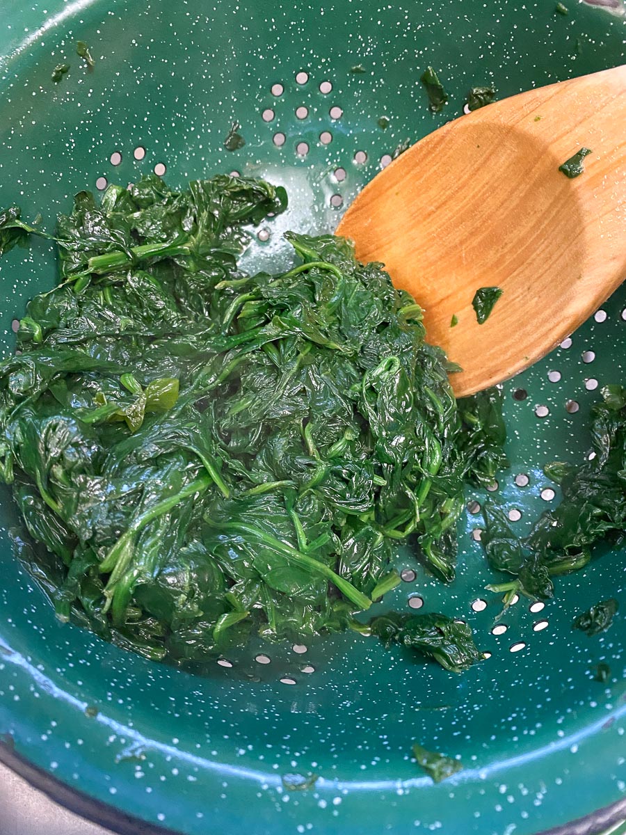 draining spinach in colander and pressing out water with wooden spoon