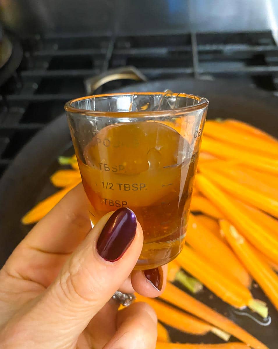 measuring cup holding honey and rice syrup, held in hand; carrots in background