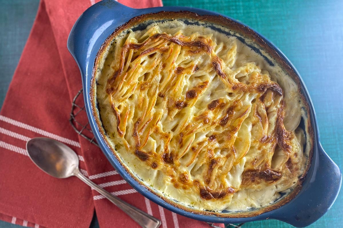 overhead image of scalloped potatoes in blue oval dish with spoon alongside