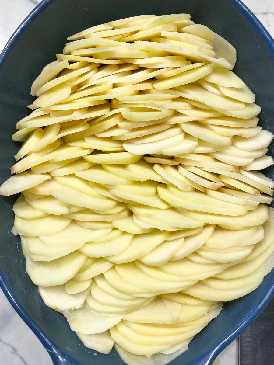 overhead image of sliced potatoes in blue casserole dish