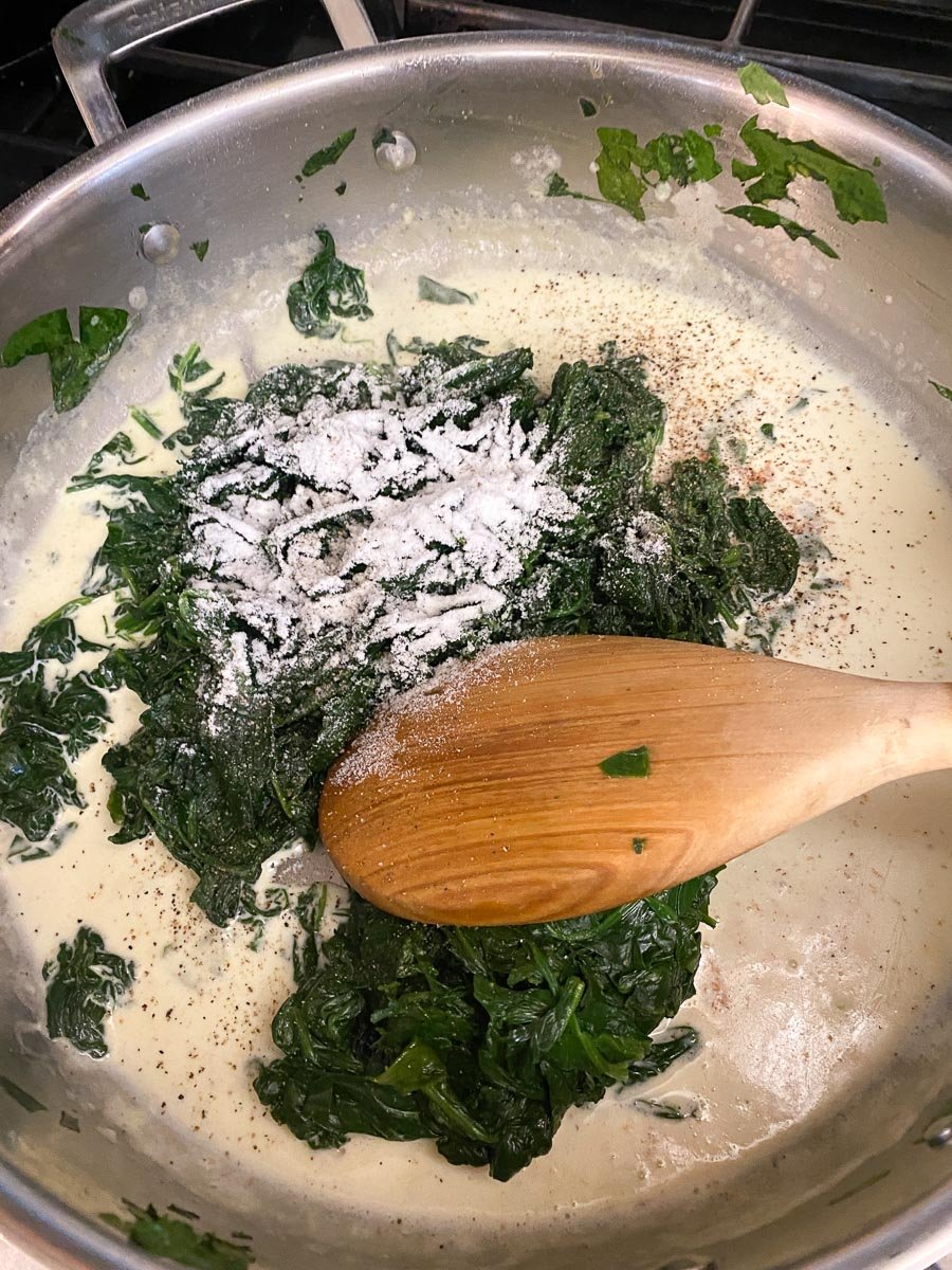 spinach and low FODMAP garlic powder added to pan with cream, stirring with wooden spoon