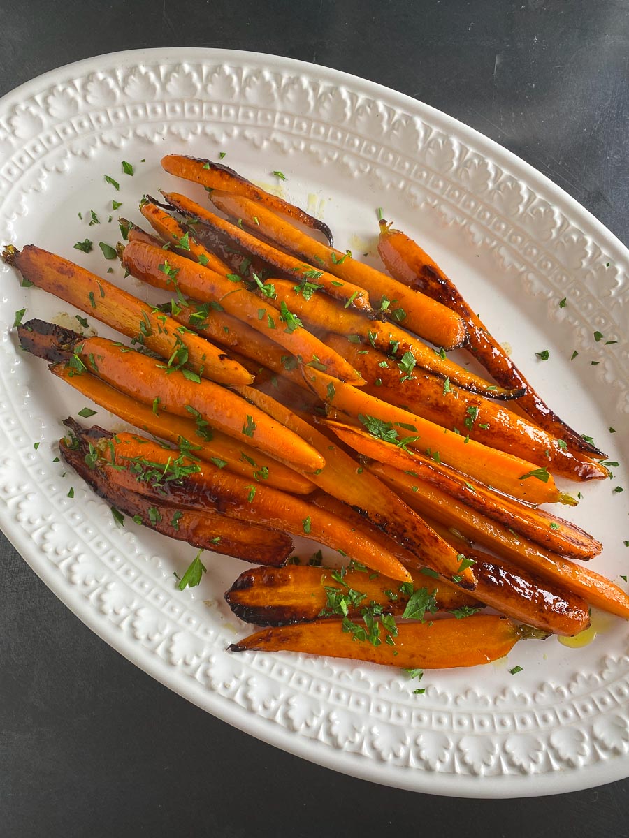 vertical image of slow FODMAP Honey Lemon Roasted Carrots in white dish, sprinkled with parsley