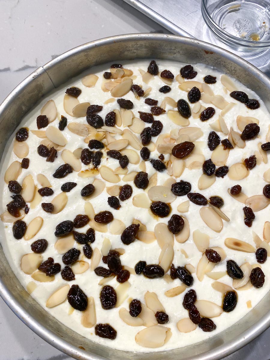 almonds and raisins on top of raw cheese cake batter in pan