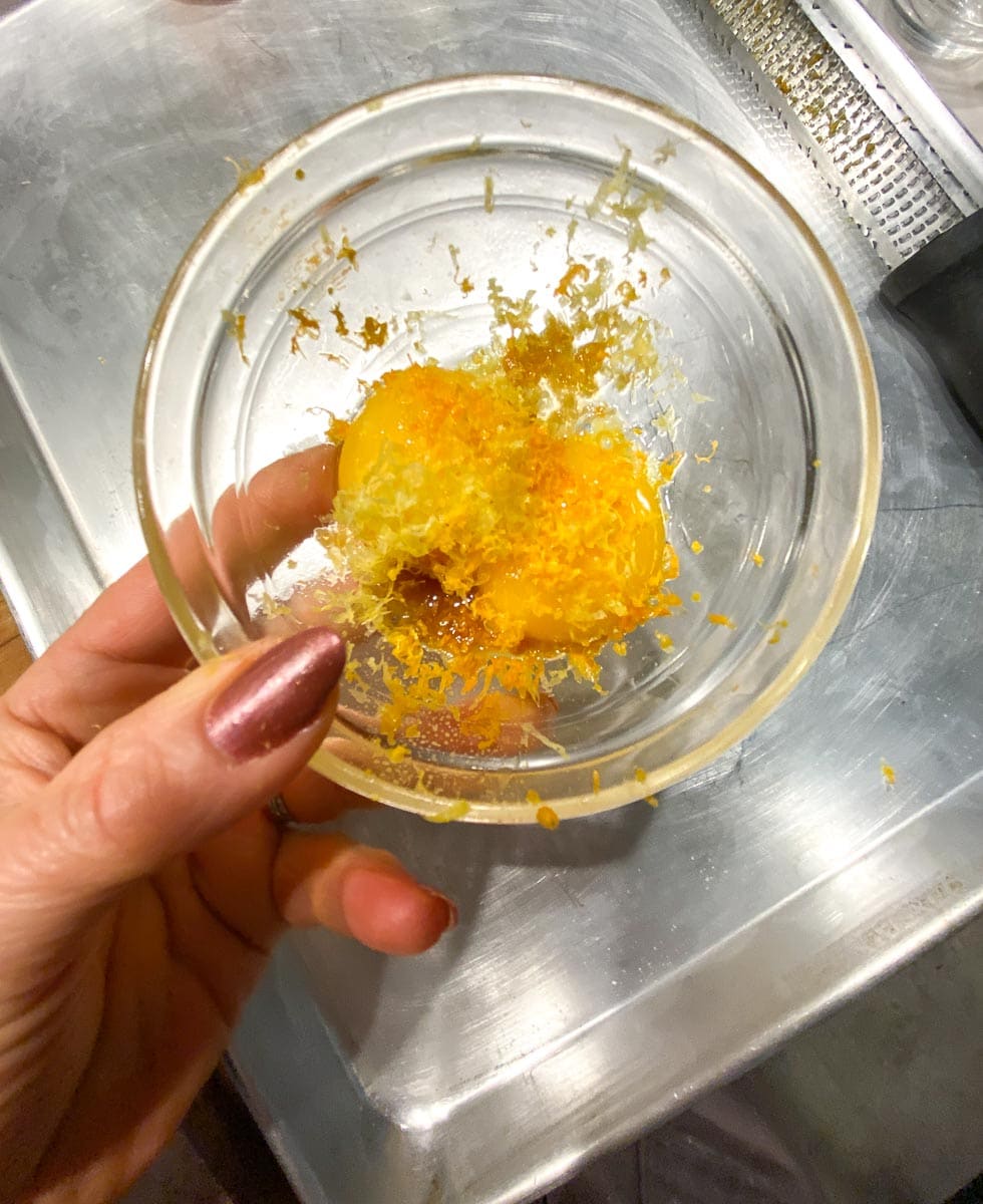 egg yolks and citrus zest in glass bowl held in hand