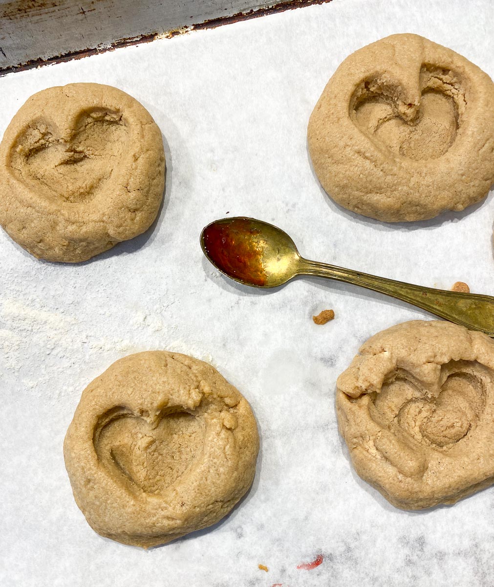forming heart shaped indentations in peanut butter cookies; demitasse spoon with jam resting on pan