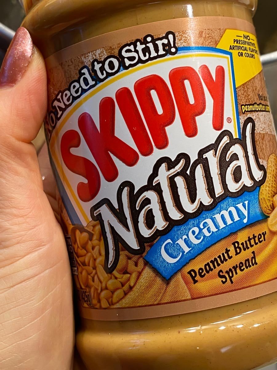 holding no stir Skippy peanut butter jar in hand showing label