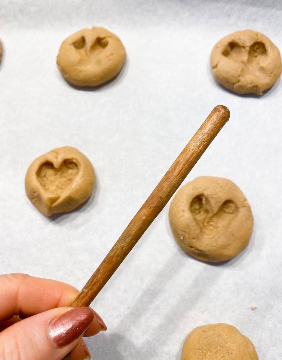 peanut butter cookies on sheet pan; hand holding wooden dowel end of wooden spoon