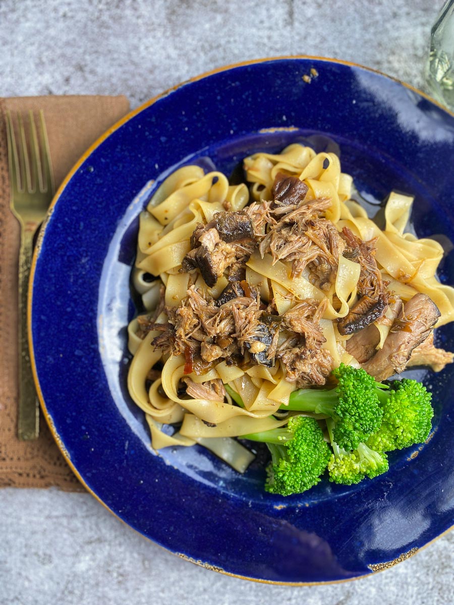 Low FODMAP Slow Cooked Asian Style Pork on blue plate with Noodles and broccoli