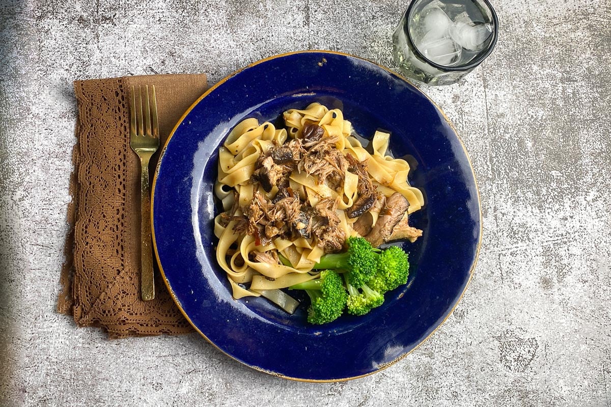 Low FODMAP Slow Cooked Asian-Style Pork with Noodles on blue plate; broccoli on the side