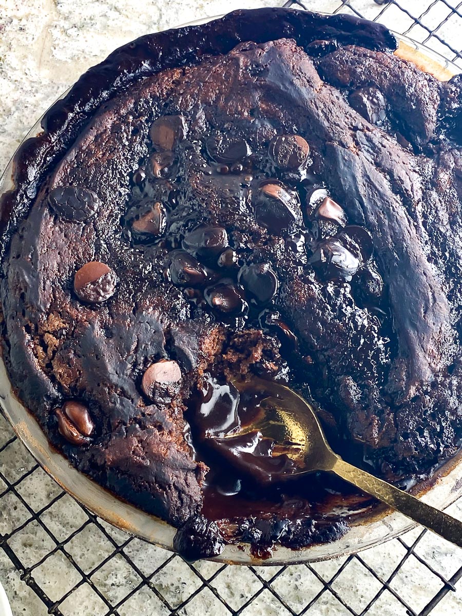 Low FODMAP chocolate Pudding Cake in pie plate on cooling rack, showing fudgy layer wit gold spoon