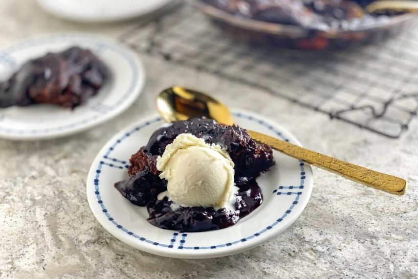 closeup Low FODMAP chocolate Pudding Cake on white plate with gold spoon and ice cream; horizontal