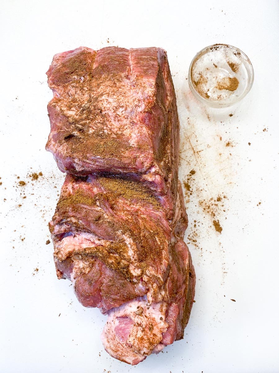 pork shoulder coated with spices on white cutting board