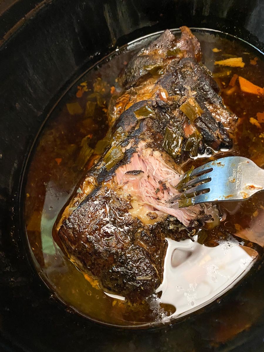 slow cooked pork being shredded with fork, in pot