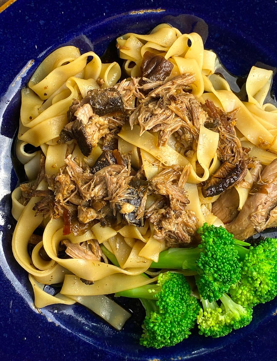 super closeup Low FODMAP Slow Cooked Asian Style Pork on blue plate with Noodles and broccoli