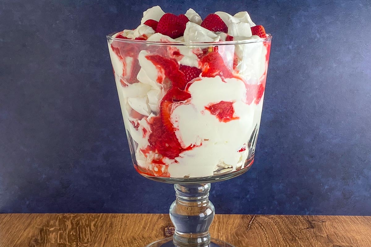 Low FODMAP Eton Mess in glass trifle bowl on wooden table, horizontal image