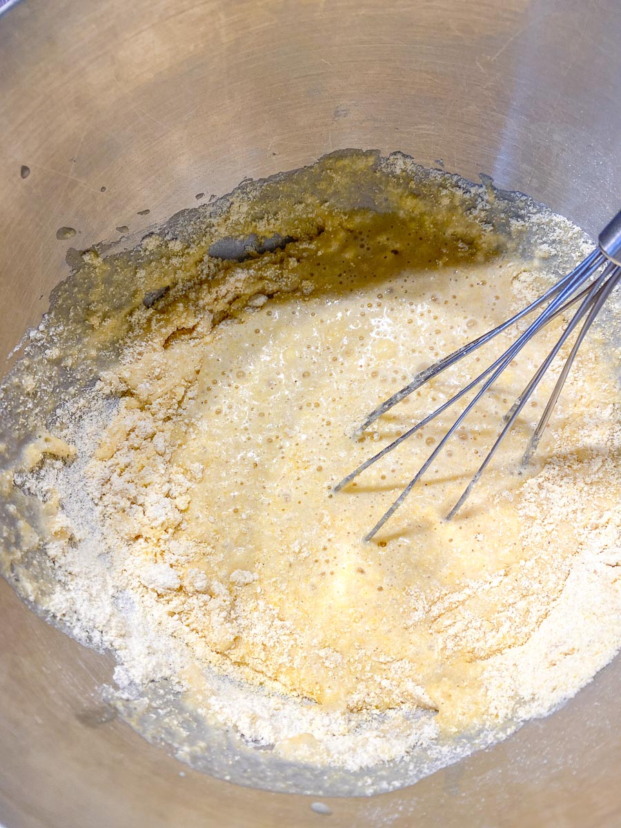 mixing wet and dry ingredents for cornbread in bowl with whisk